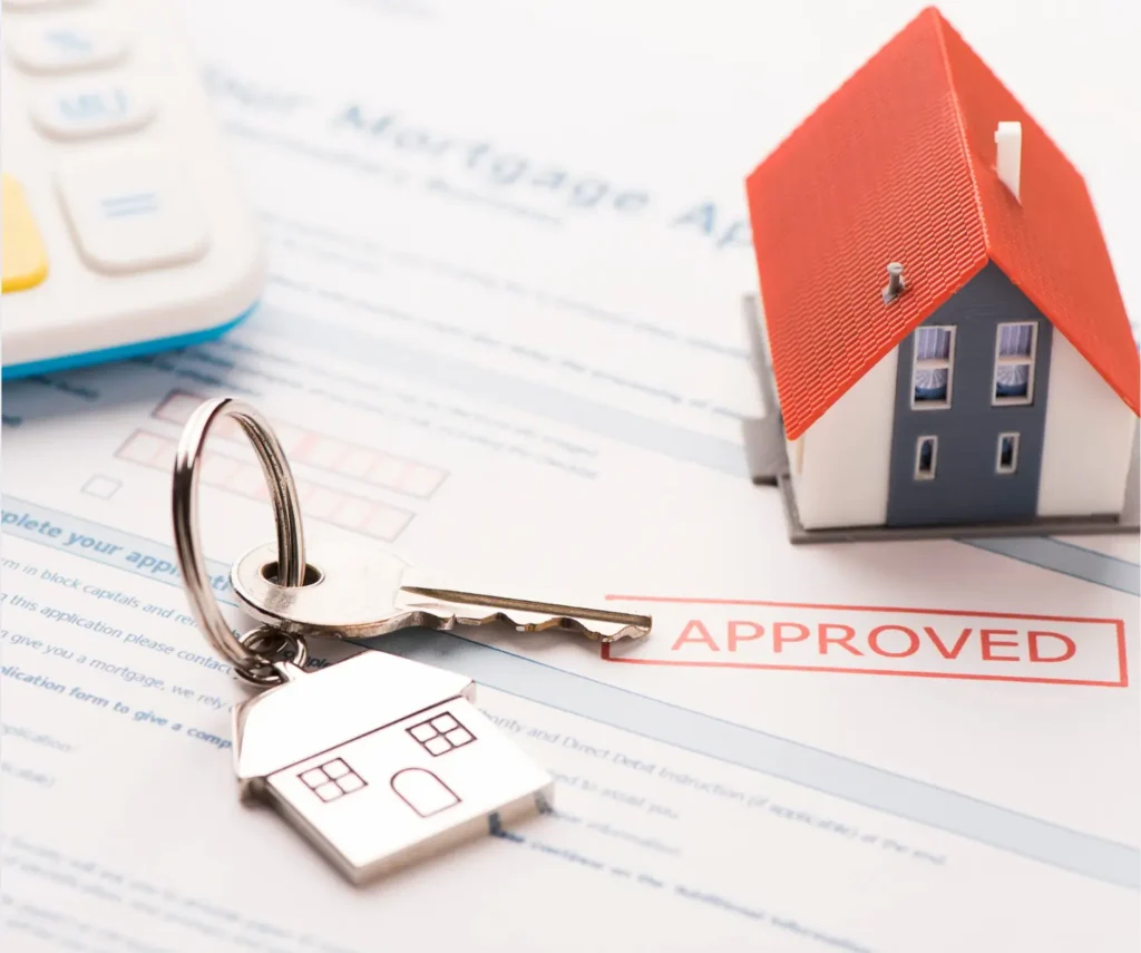 A model house with a red roof next to a key on a mortgage application marked 'APPROVED'.